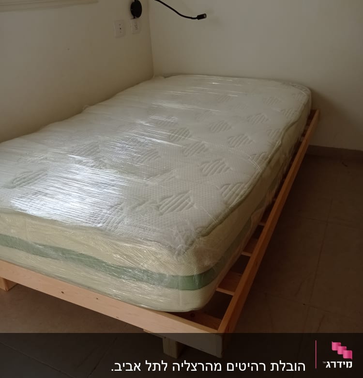 מזרן עטוף בניילון על מיטת עץ בחדר ריק